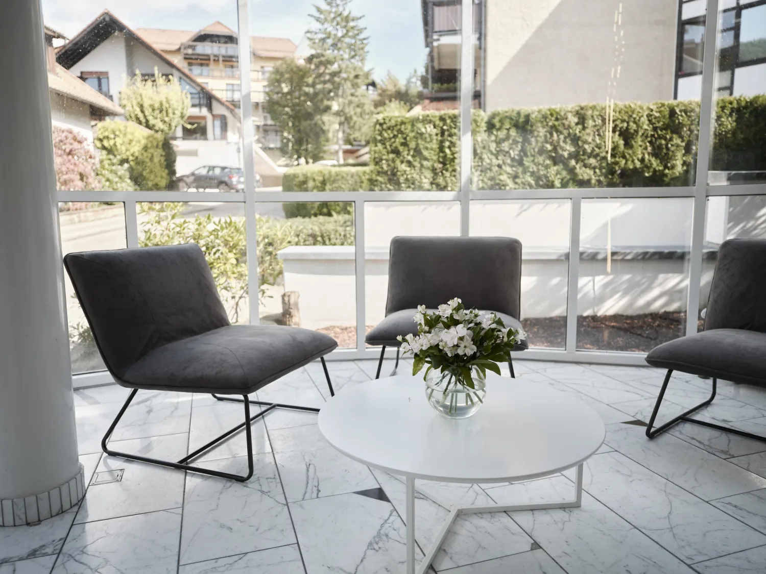 Loungesessel um einen runden Tisch vor verglaster Front