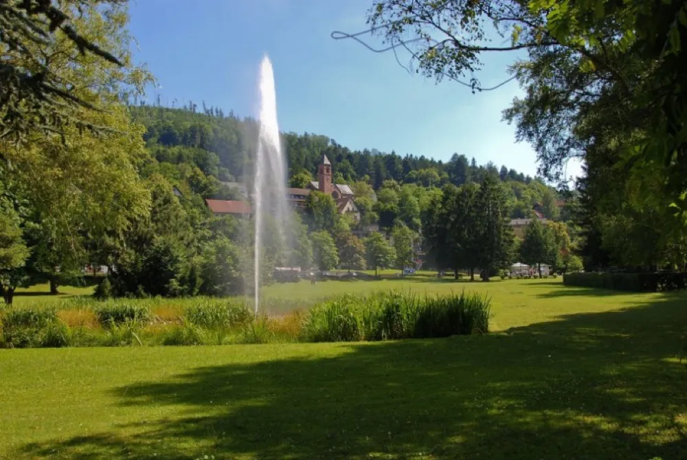 Der Kurpark von Bad Herrenalb im Sommer mit der bekannten Wasserfontäne und der Klosterkirche im Hintergrund