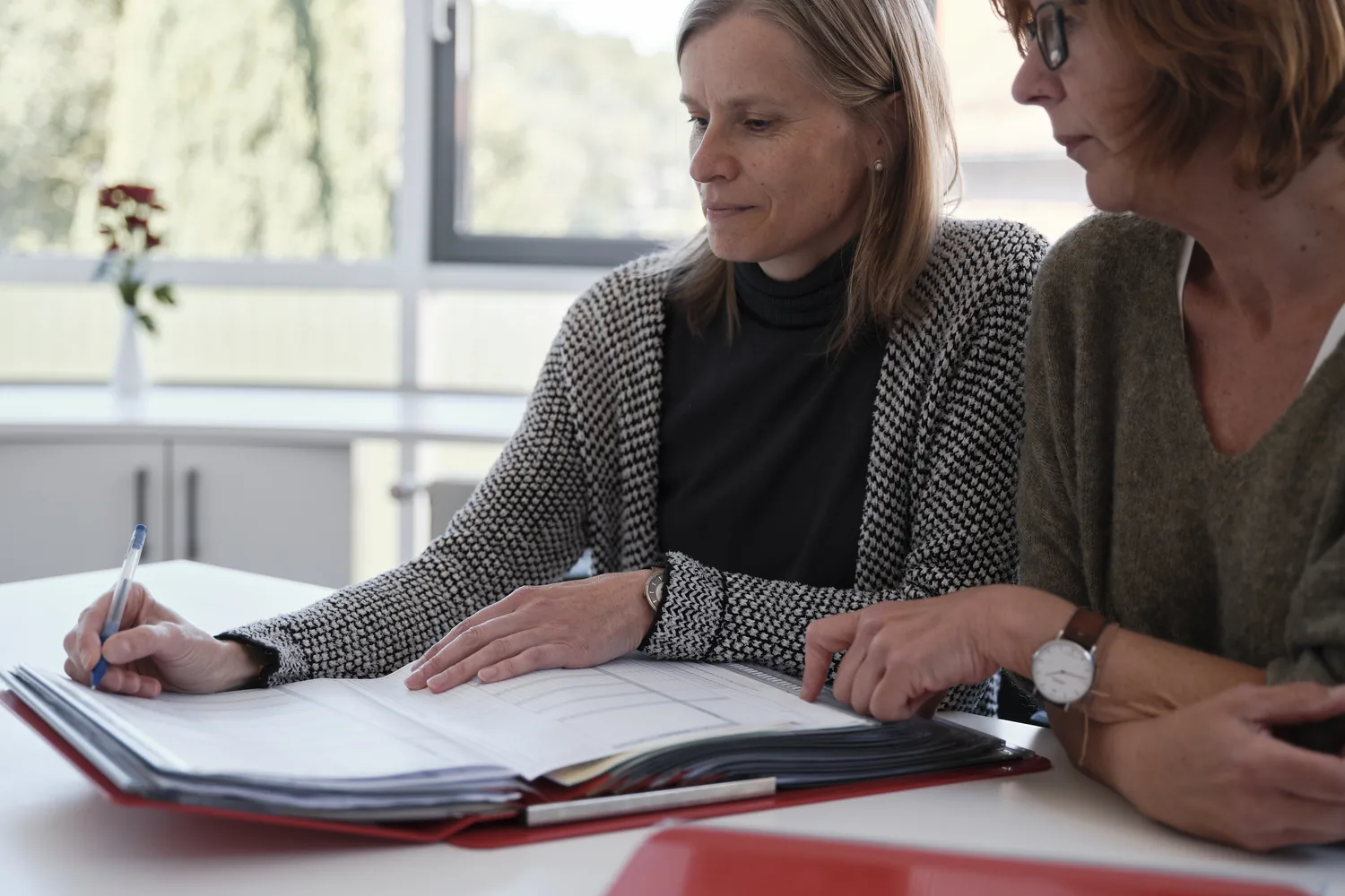 Zwei Frauen besprechen gemeinsam einen aufgeschlagenen Ordner am Tisch