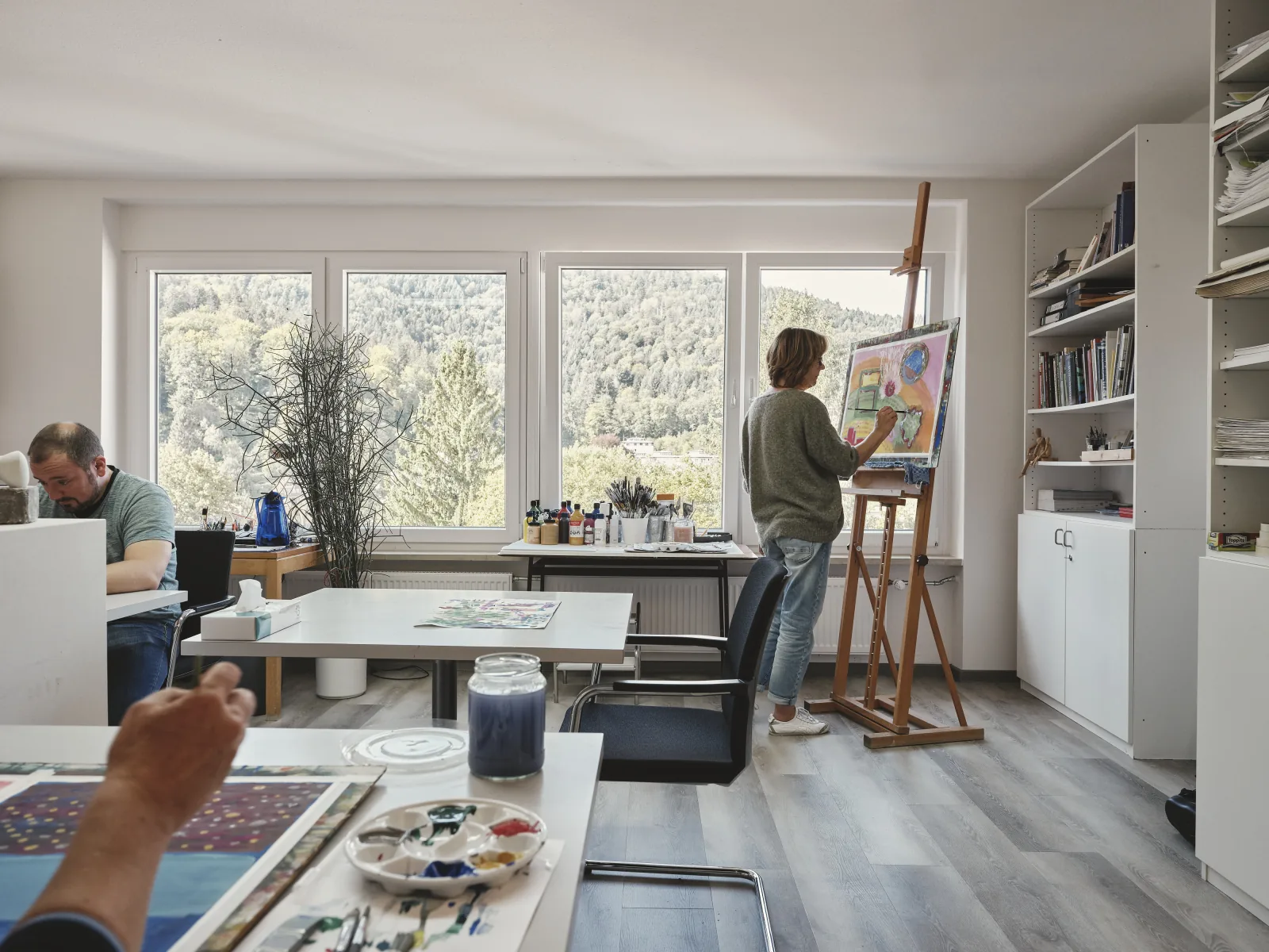 Kunsttherapie-Atelier mit Blick ins Grüne — Patientin malt an der Staffelei in der Sanima Klinik am Mayenberg