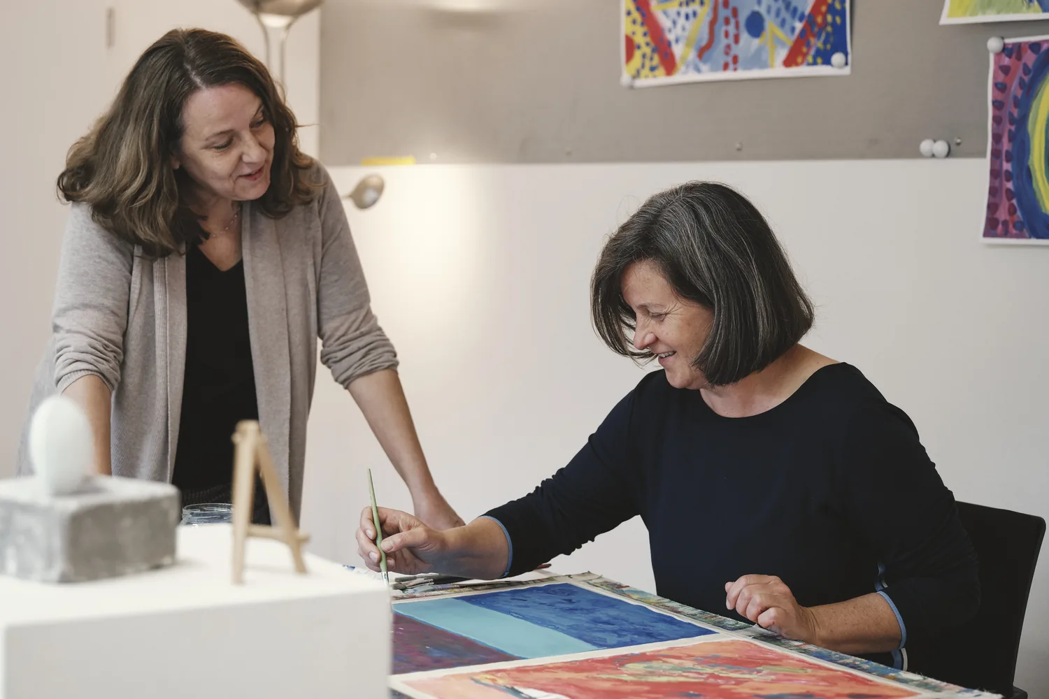 Zwei Frauen arbeiten am Tisch an einem Kunstwerk in der Kunsttherapie