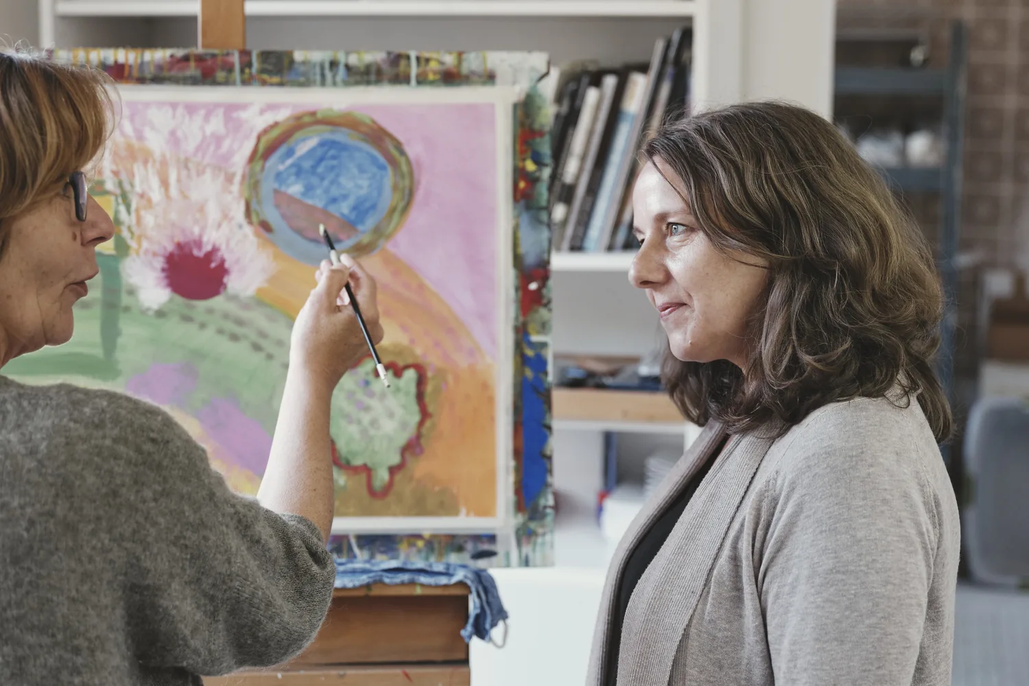 Pinsel deutet auf ein rundes Mandala-Motiv auf einer farbigen Leinwand