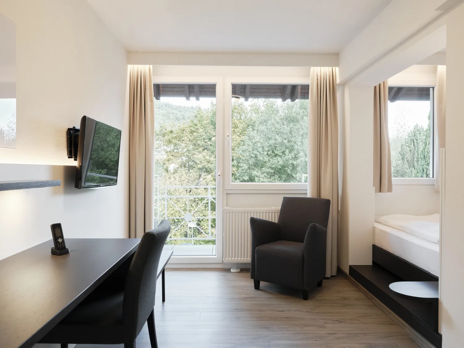 Helles Patientenzimmer mit Schreibtisch, Sessel und bodentiefem Fenster