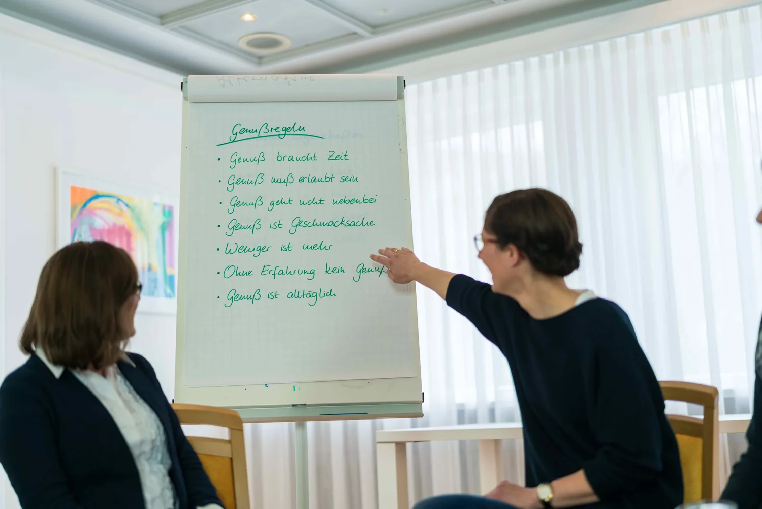 Therapeutin erläutert am Flipchart, zwei Teilnehmerinnen hören zu